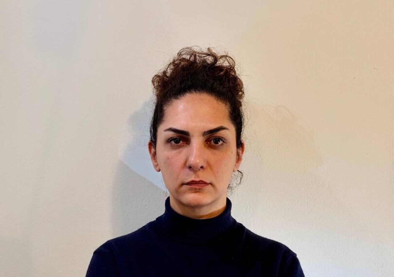 Baharak Abdolifard in schwarzem Pulli vor weißer Wand, sie verschränkt die Arme und blickt ernst.