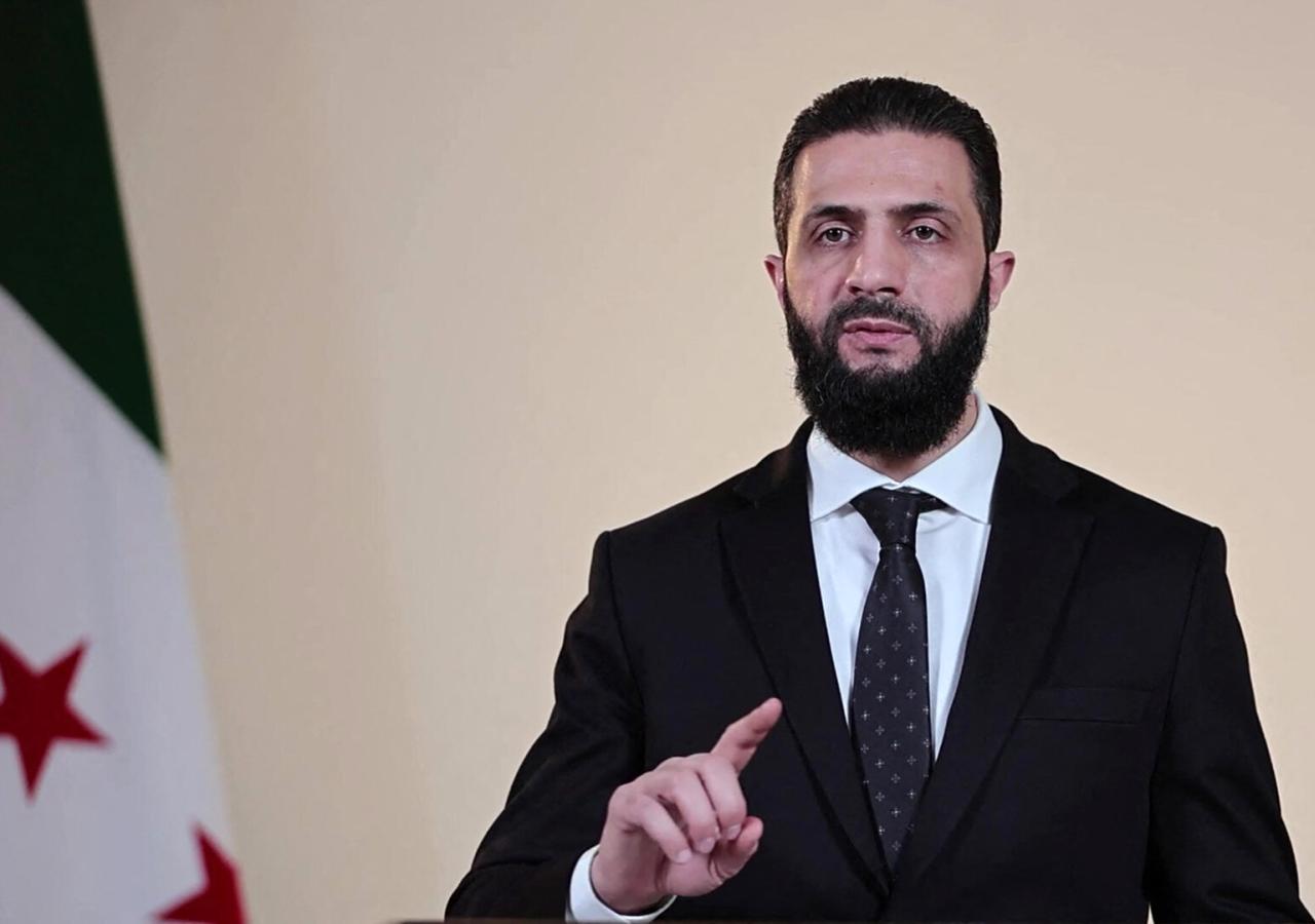 Ahmed al-Scharaa in Anzug, links Syrien-Flagge