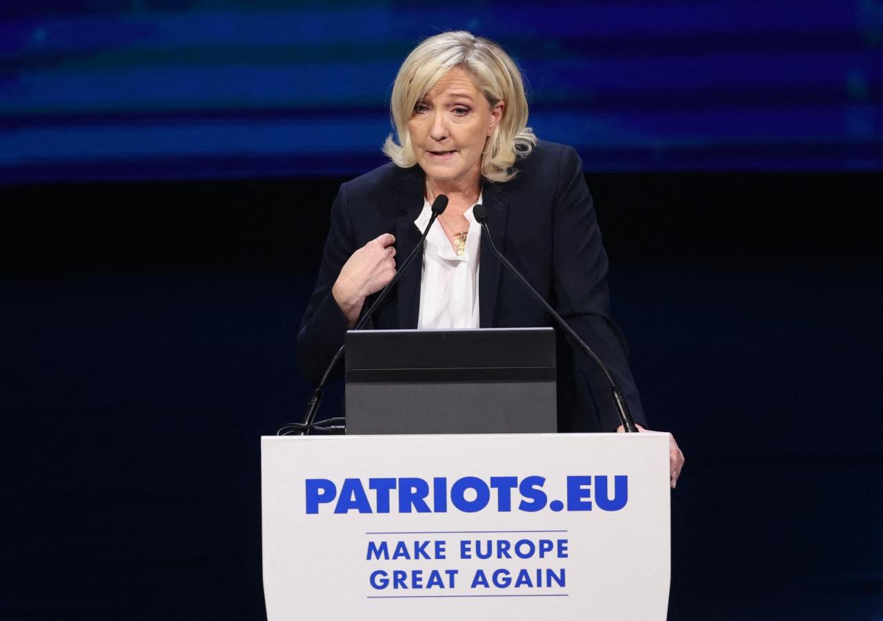 Marin Le Pen spricht auf einem Podium, man kann den Schriftzug "patriots.eu" lesen.