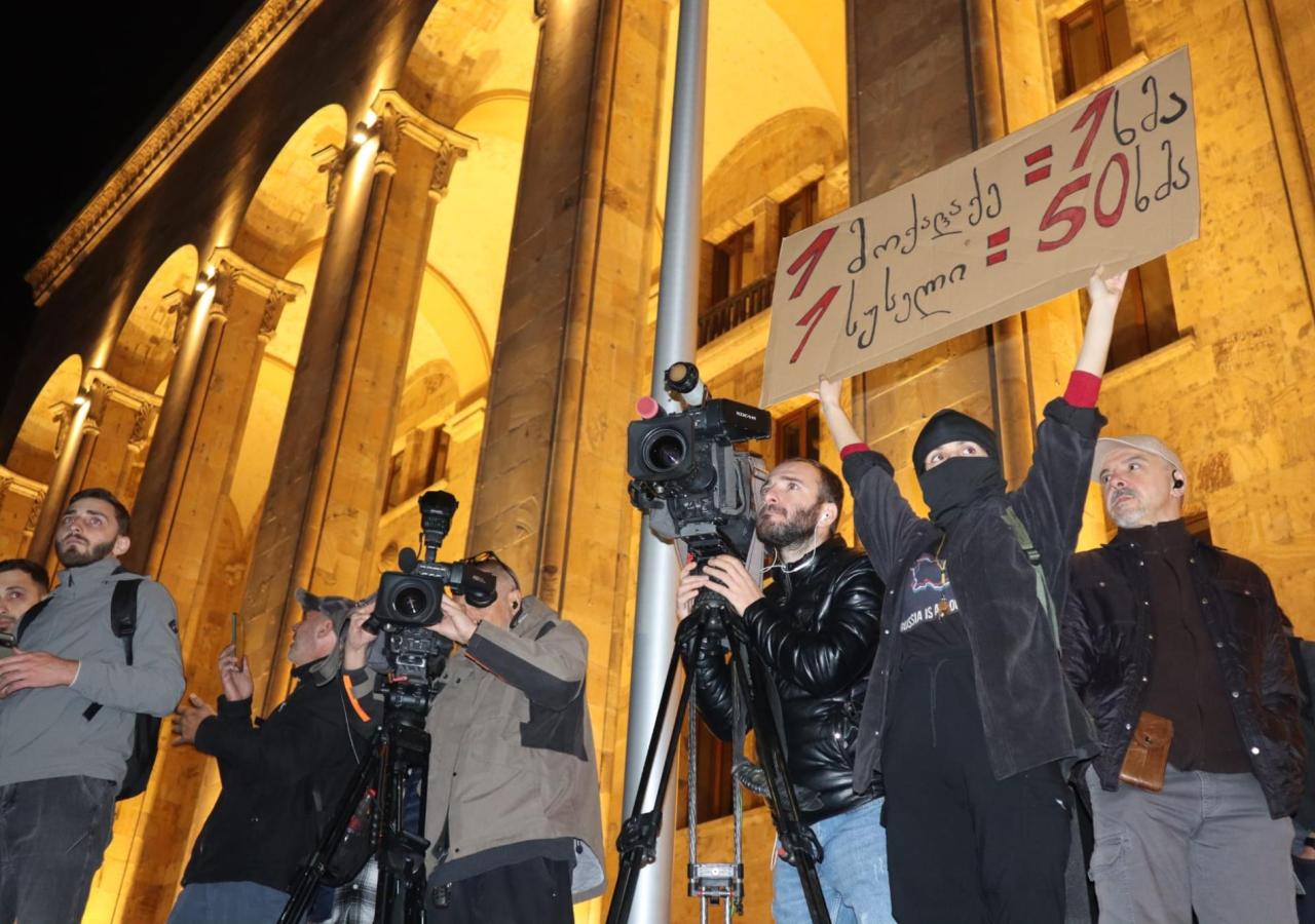 Eine Frau hält ein Schild vor dem Parlament hoch, neben ihr stehen Kameramänner.