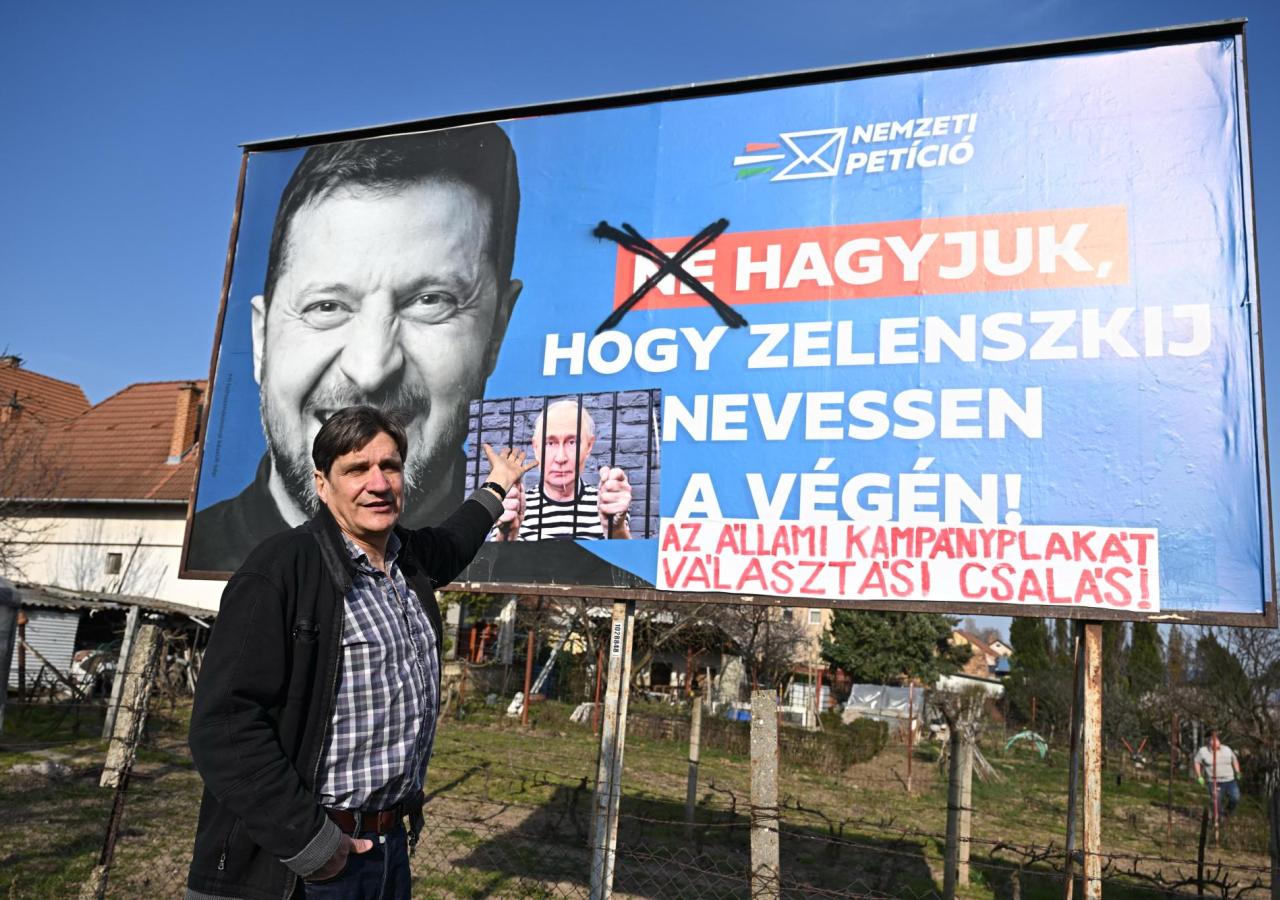 Ein Mann steht vor einem Fidesz-Poster mit einem lächelenden Wolodymyr Selenskyj darauf.