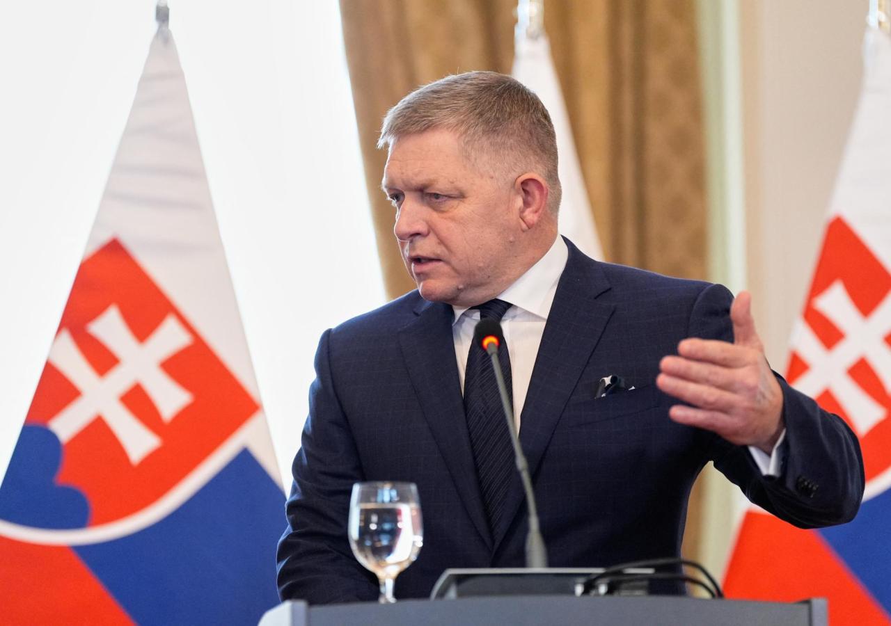 Robert Fico spricht auf einer Pressekonferenz in ein Mikro, hinter ihm slowakische Flaggen.