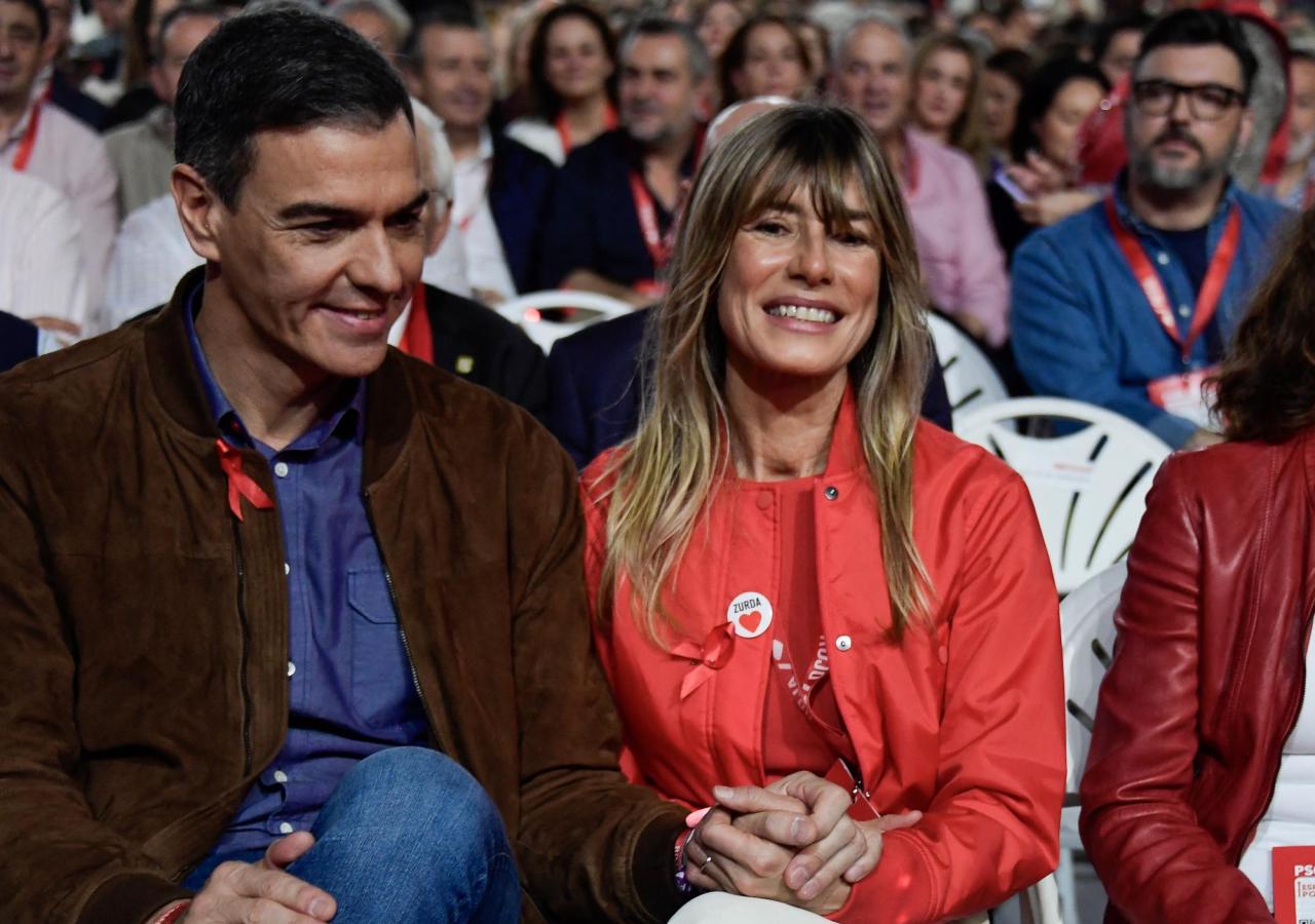 Pedro Sánchez und seine Ehefrau Begoña Gómez sitzen bei einer Veranstaltung auf weißen Plastiksesseln.