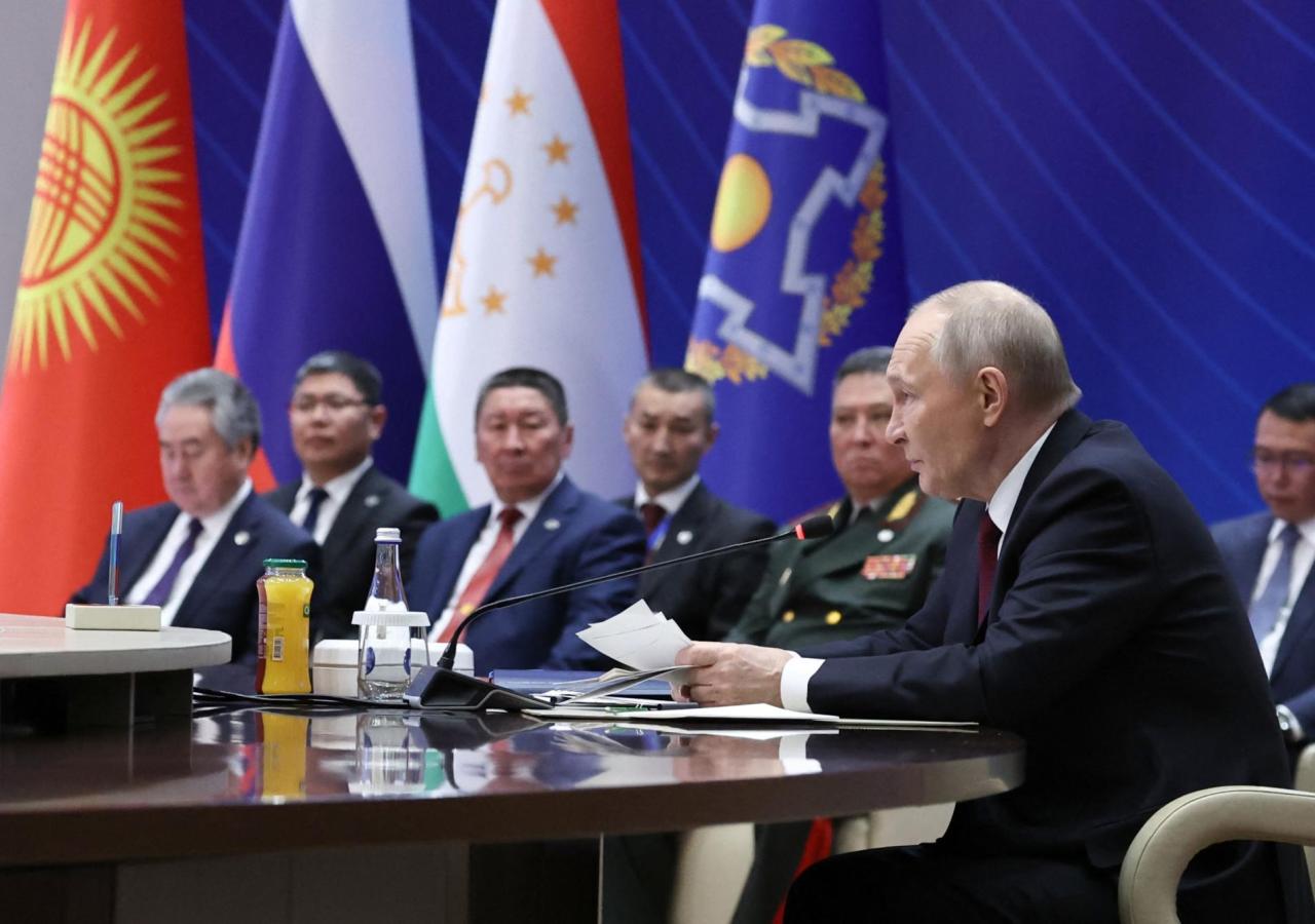 Wladimir Putin sitzt an einem Tisch, dahinter Generäle und die Flagge von Kirgisistan, Russland, Tadschikistan und der OVKS.