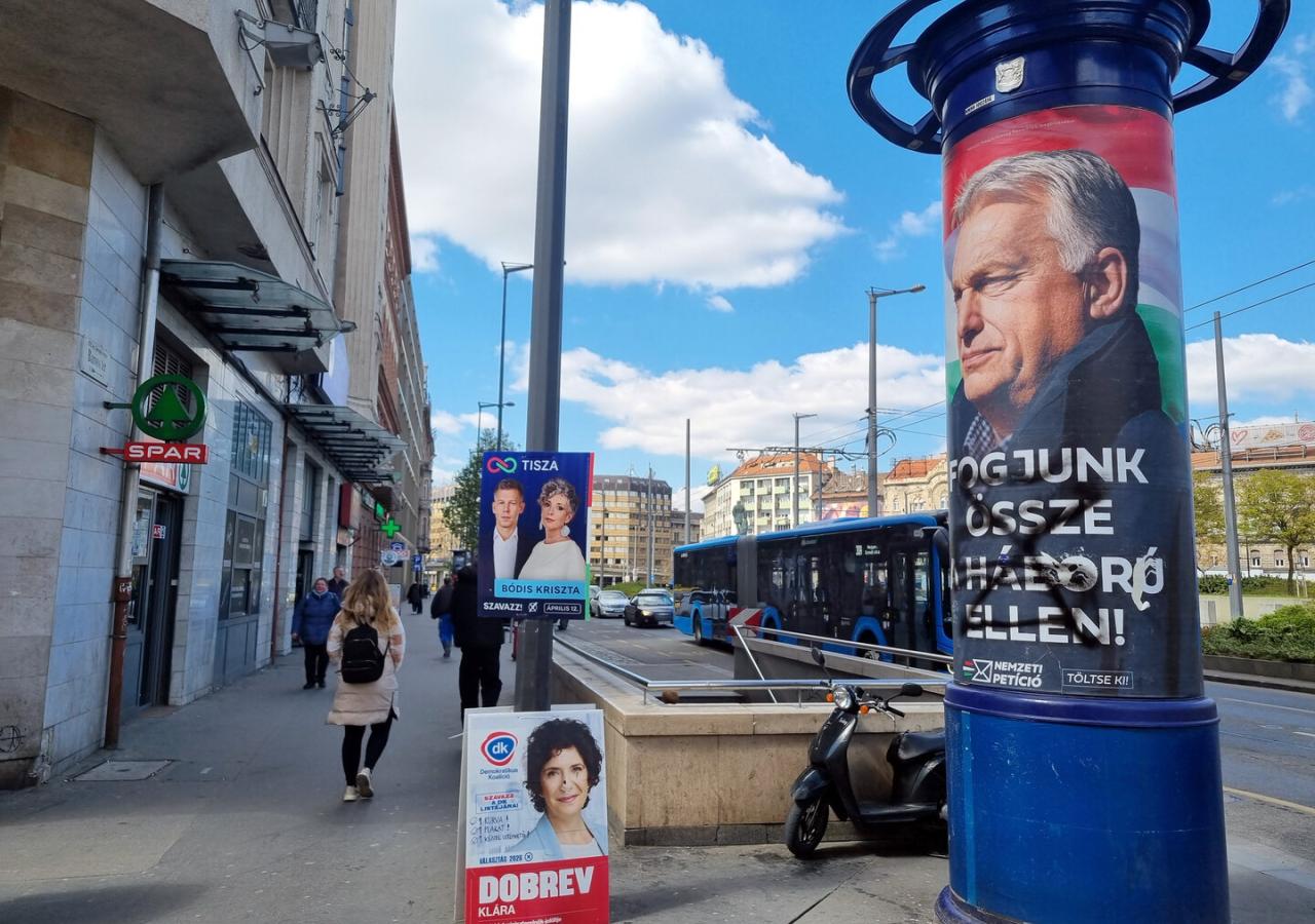Litfaßsäule mit Viktor Orbáns Konterfei, sie ist beschmiert. Daneben kleinere Plakate von Peter Magyar und der Partei DK.