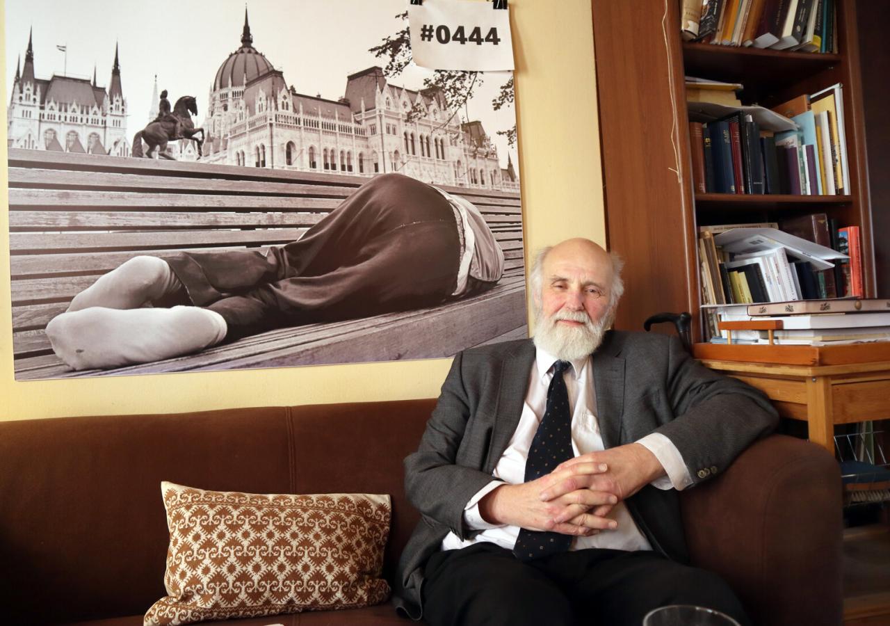 Gabor Ivanyi sitzt auf einem braunen Sofa, dahinter ein Bild eines Obdachlosen, der vor einem Prachtbau schläft.