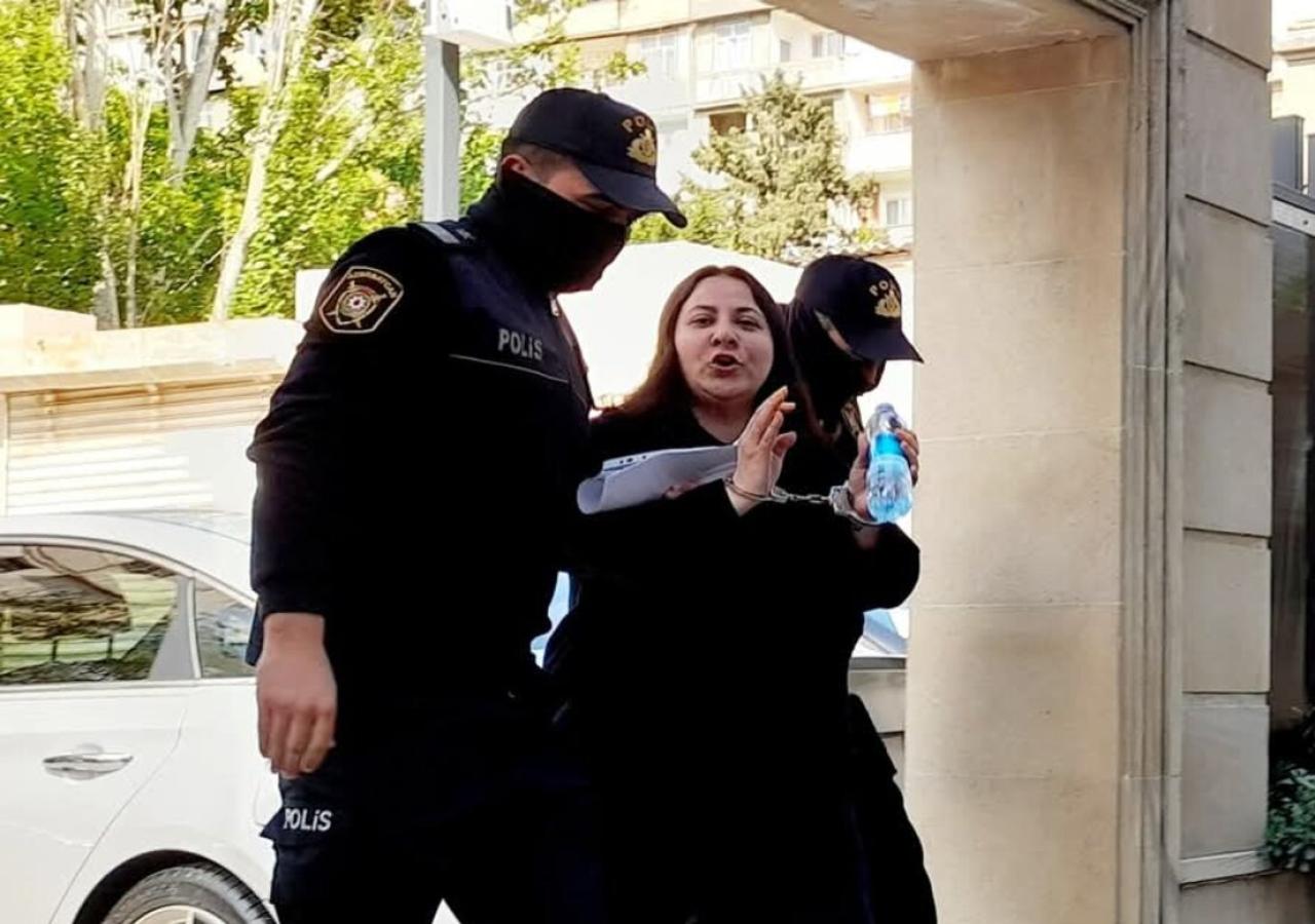 Zwei vermummte Polizisten führen Guliyeva, der Handschallen umgelegt wurden, durch ein Tor.