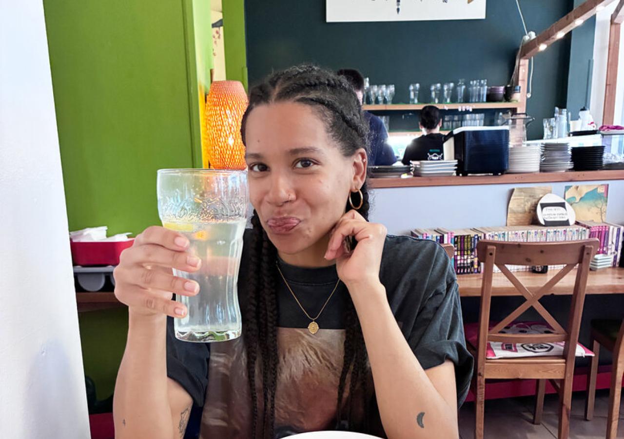 Rebecca Horner sitzt an einem Tisch, vor sich asiatische Speisen, in der Hand ein großes Glas Soda-Zitron