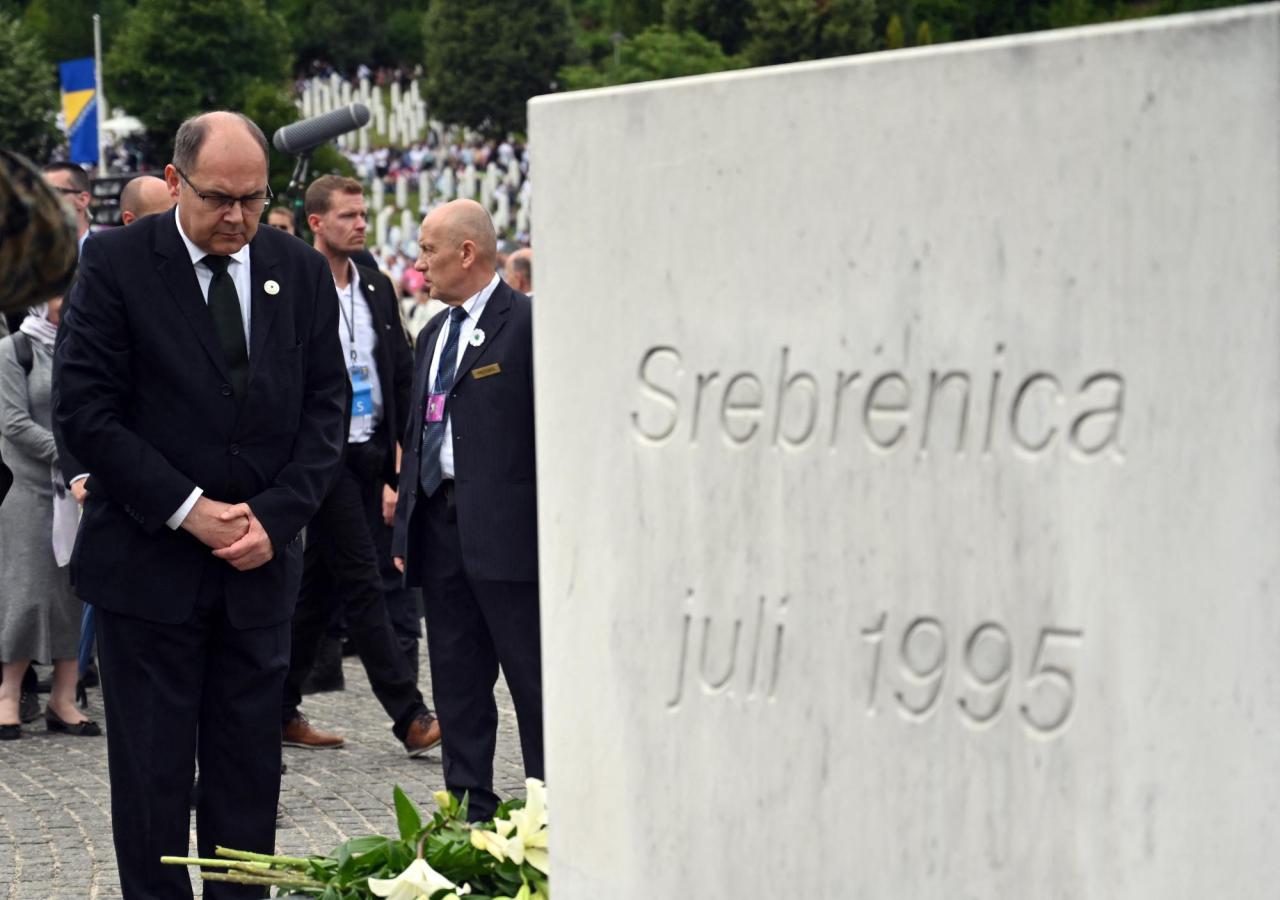 Bosnien-Repräsentant Christian Schmidt steht vor einem Stein mit der Aufschrift "Srebrenica juli 1995" und blickt auf den Boden, während er die Hände gefaltet hält.