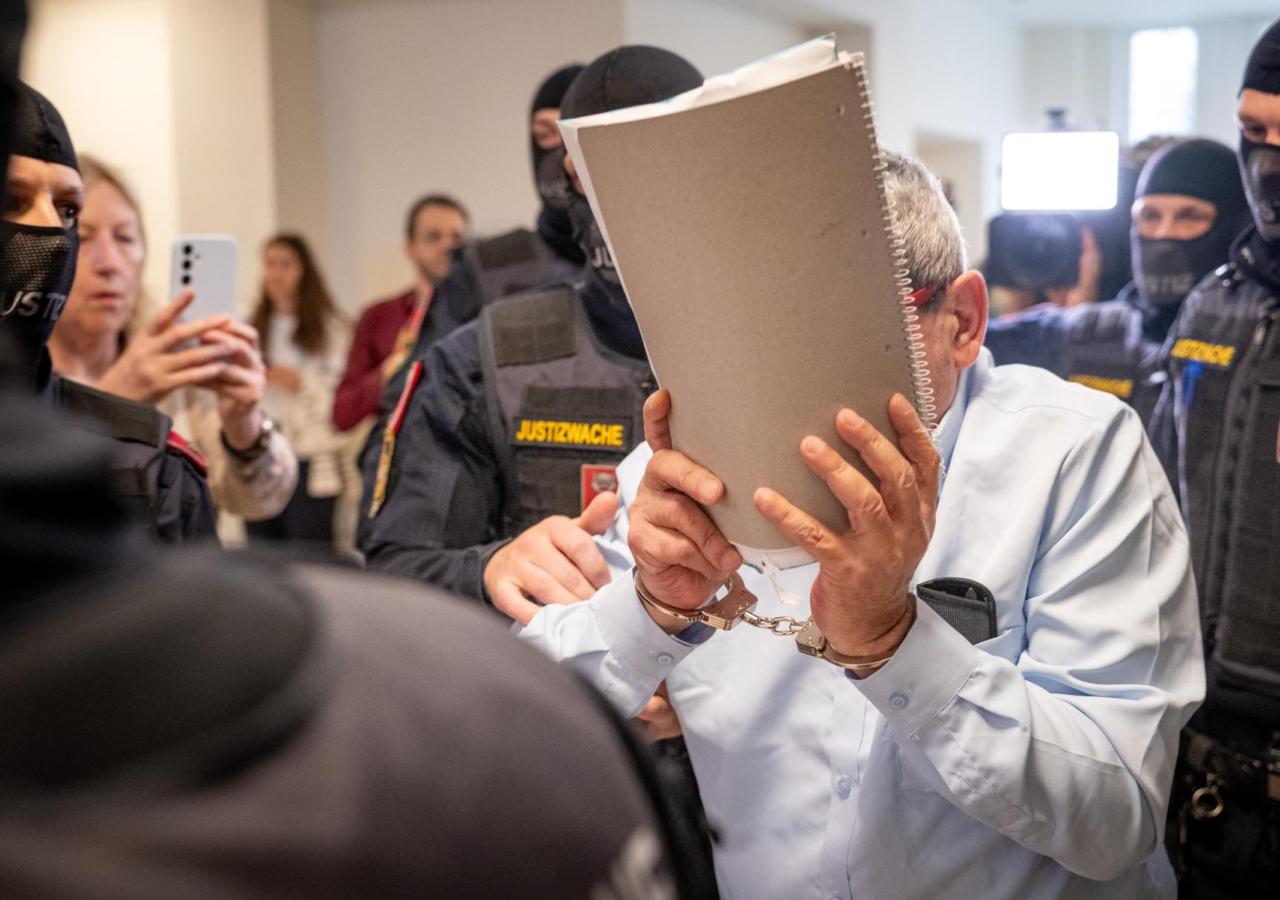 Khaled H. verdeckt sein Gesicht mit einer Mappe, er ist umringt von Polizeibeamten.