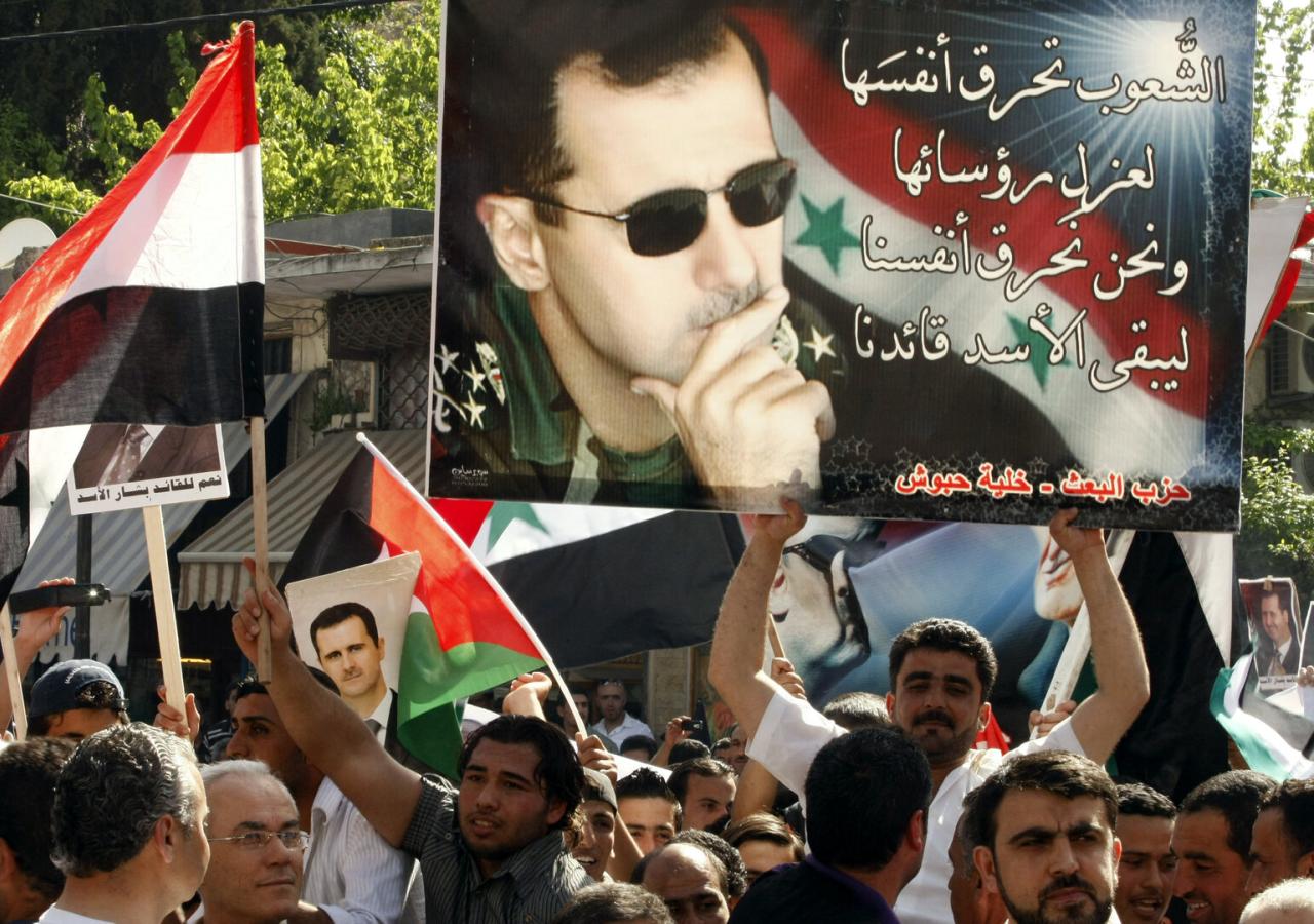 Demonstrierende halten ein Plakat mit Baschar Al Assad hoch.