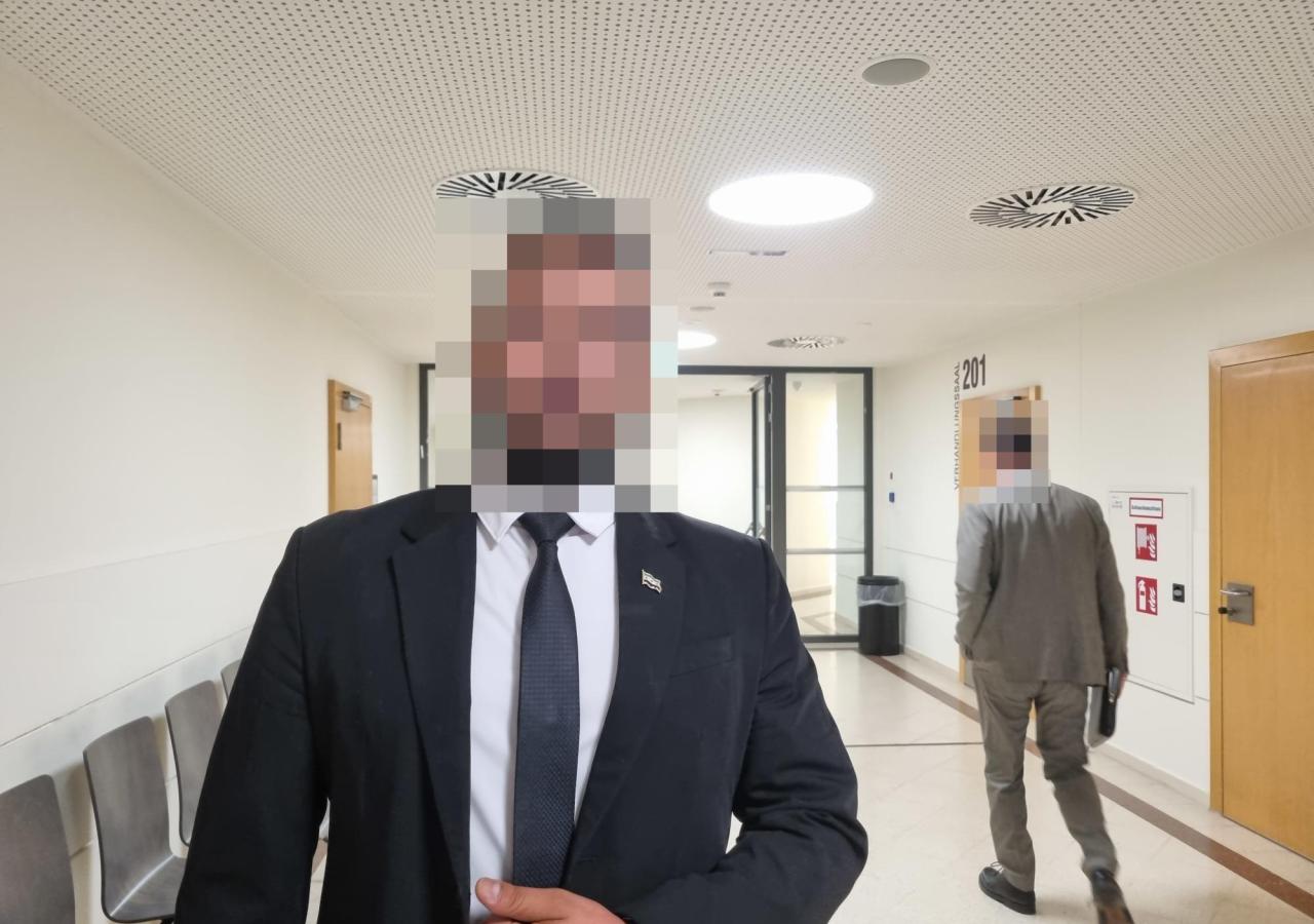 Zeuge Achmad in Anzug in einem Gang des Wiener Landesgericht, sein Gesicht ist verpixelt.