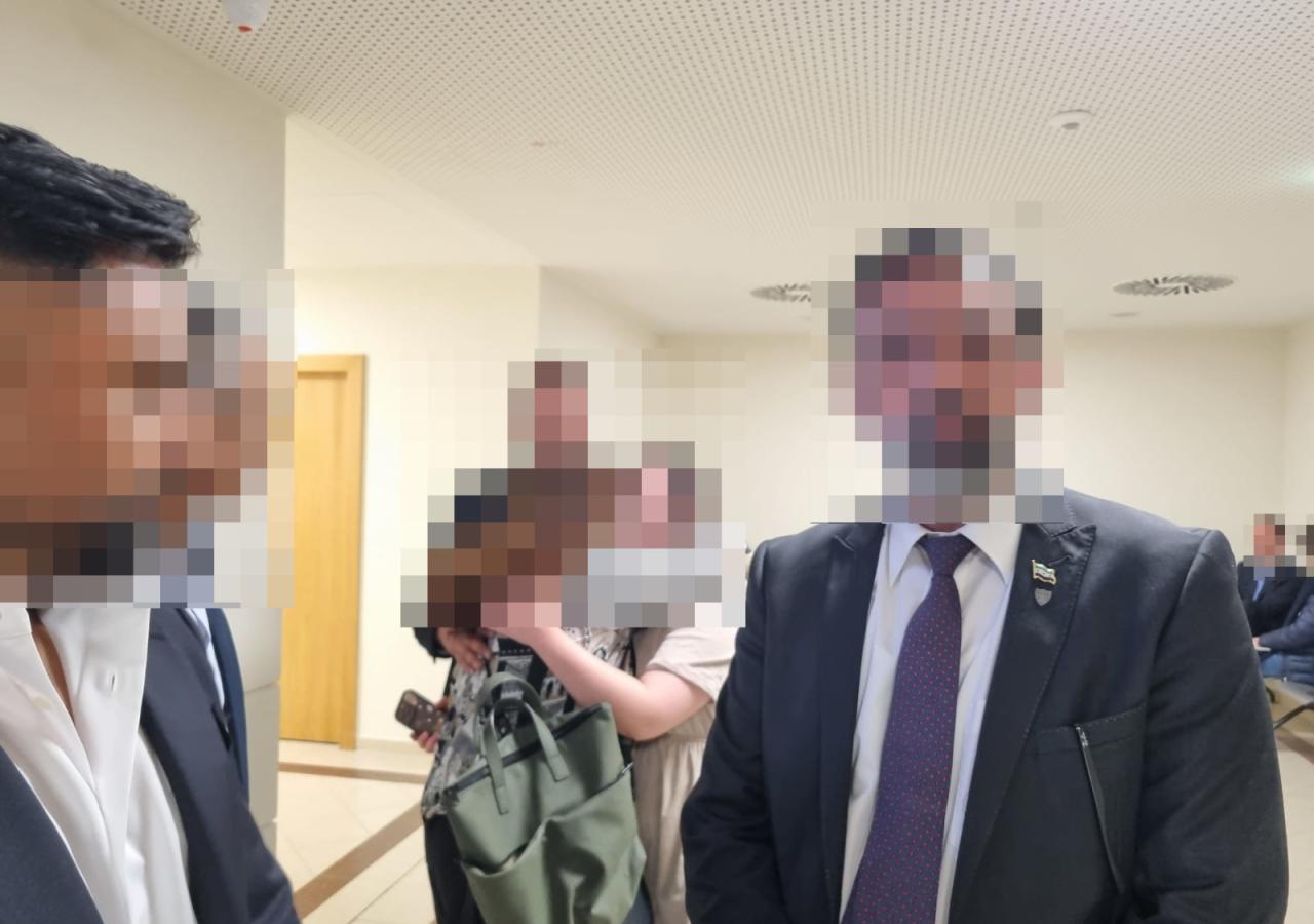 Eine Personengruppe steht in einem Gang am Gericht, dahinter umarmen sich drei Menschen.