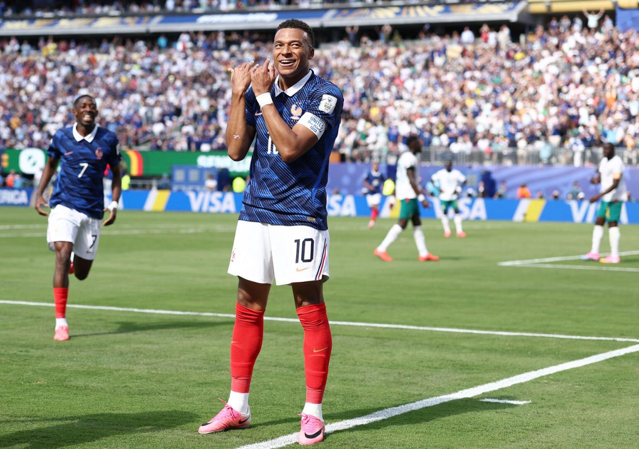 Kylian Mbappe steht auf dem Fußballplatz und jubelt über ein Tor, indem er eine Flötenbewegung macht