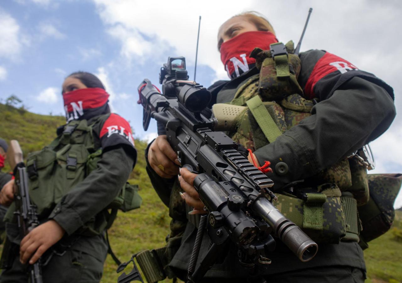 Zwei Frauen stehen mit Maschinengewehren da, sie tragen Armbänder mit der Aufschrift "ELN".