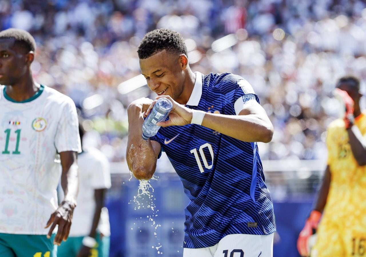 Kylian Mbappe schüttet sich während eines Fußballspiels Wasser aus einer Trinkflasche auf den Arm