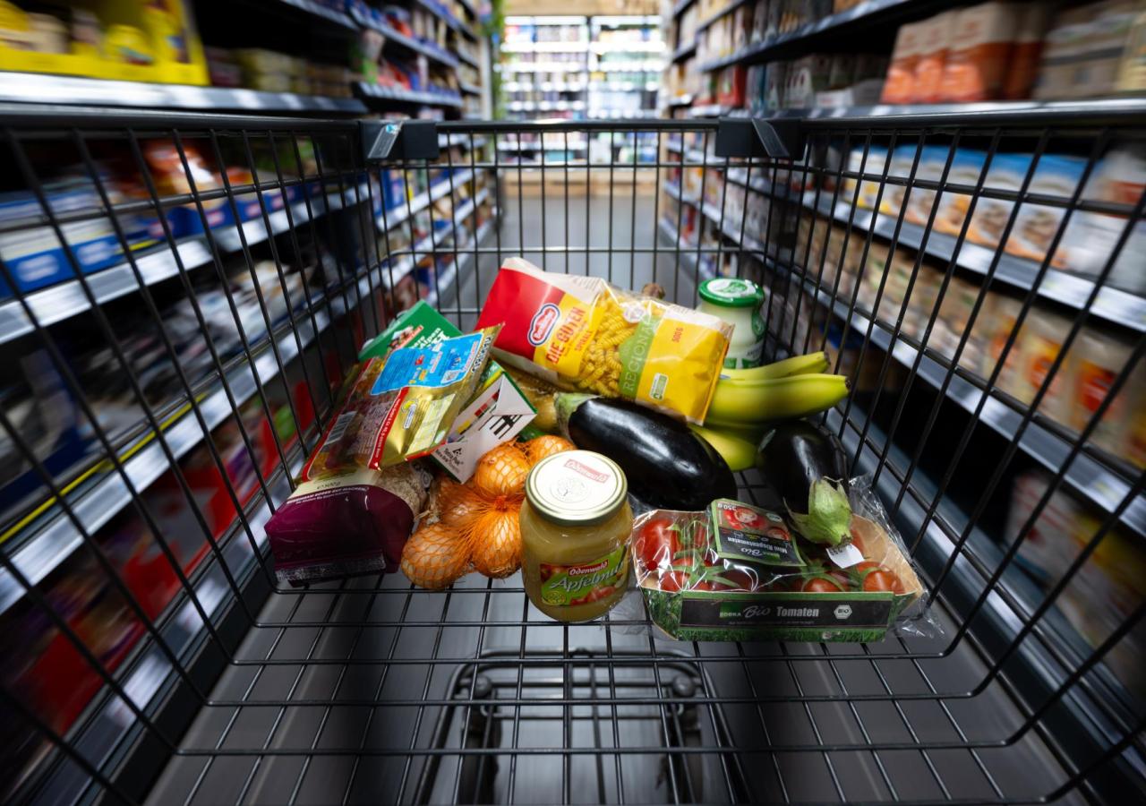 Einkaufswagen mit Produkten wird durch Supermarkt geschoben.
