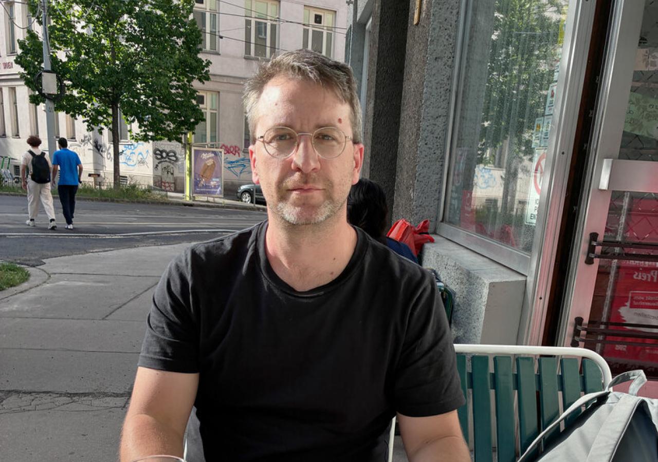 Ein Mann mit Brille und schwarzem T-Shirt sitzt vor einem Schmalzbrot und einem großen Bier
