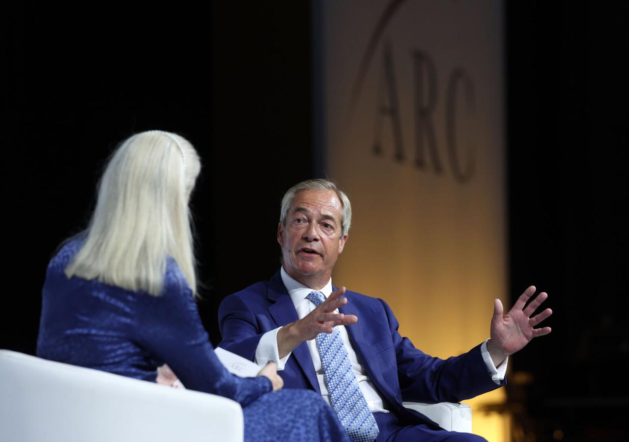Nigel Farage sitzt auf einer Bühne und gestikuliert, er redet mit Philippa Stroud (Tories und ARC).