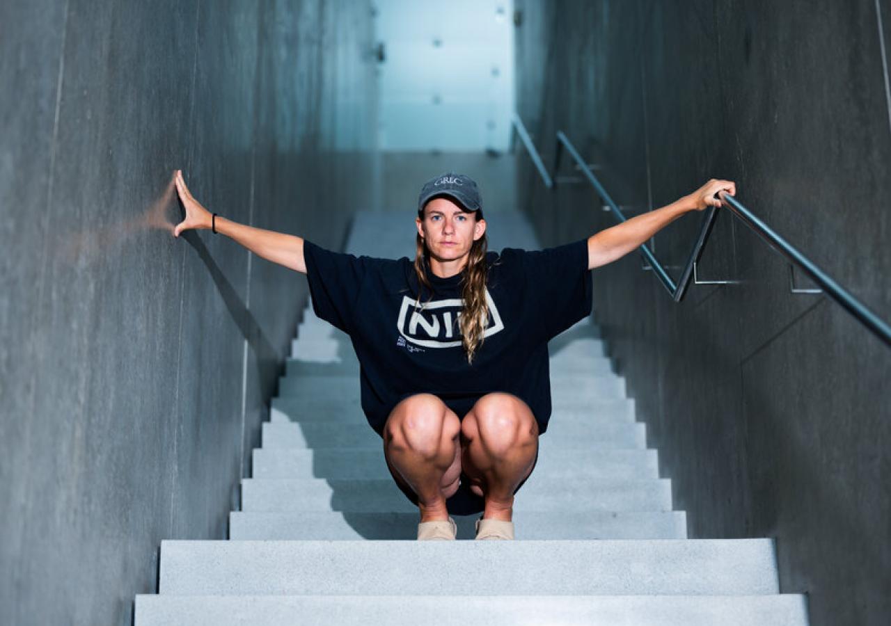 Die Künstlerin Florentina Holzinger mit ausgebreiteten Armen, in der Hocke, auf einer steilen Treppe im Kunsthaus Bregenz, fotografiert von Wolfgang Paterno
