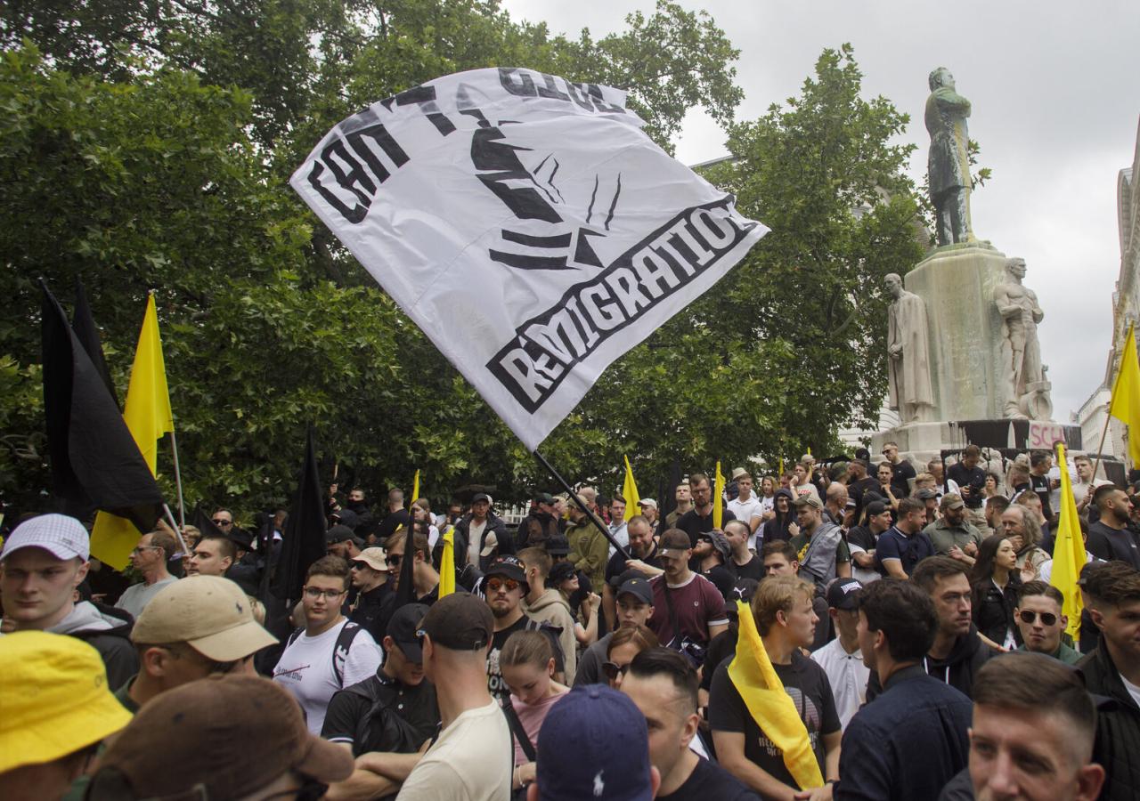Menschenmenge bei einer Demonstration mit schwarzen und gelben Fahnen vor einem Denkmal.