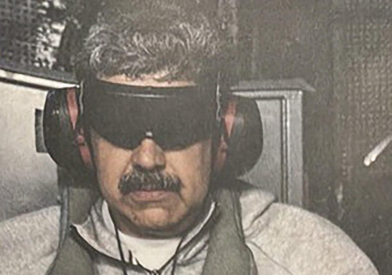 Nicolás Maduro in Gefangenenkleidung, er trägt eine schwarze Brille.