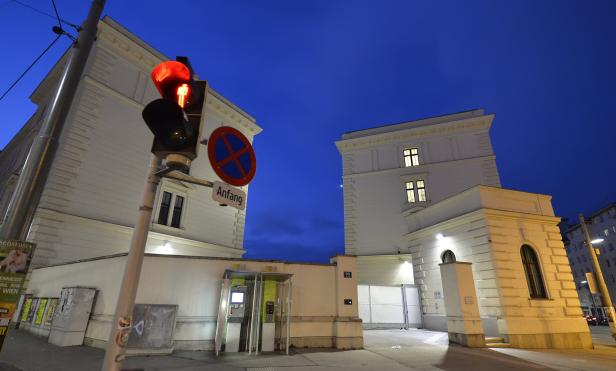 Eine rote Fußgängerampel vor zwei weißen Gebäuden in Wien bei Nacht.