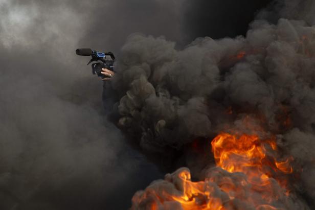 Ein Journalist filmt unter brennenden Reifen, die während einer Demonstration in der südirakischen Stadt Basra von regierungsfeindlichen Demonstranten angezündet wurden. Ein Journalist filmt unter brennenden Reifen, die während einer Demonstration in der südirakischen Stadt Basra von regierungsfeindlichen Demonstranten angezündet wurden.