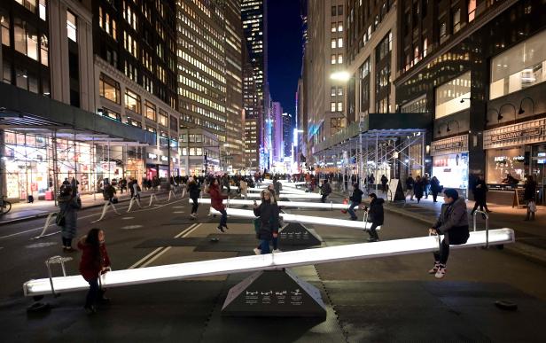 Menschen schaukeln auf leuchtenden Wippen, einer Installation namens „Impulse“, die sich am Broadway in der Nähe des Time Square in New York City befinden. Menschen schaukeln auf leuchtenden Wippen, einer Installation namens „Impulse“, die sich am Broadway in der Nähe des Time Square in New York City befinden.