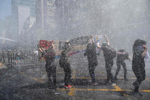 Die Demonstranten werden von der Bereitschaftspolizei in Santiago am sechsten Tag in Folge mit Wasser bespritzt. Ein vierjähriges Kind wurde bei den jüngsten Protesten gegen die wirtschaftliche Ungleichheit in Chile getötet und die Zahl der Todesopfer erh