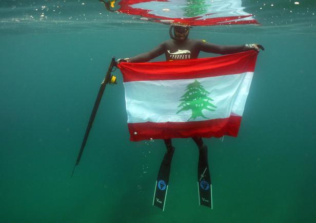 Ein Taucher nimmt eine libanesische Nationalflagge unter Wasser vor dem Ufer der nördlichen Stadt Qalamun mit, in Solidarität mit den anhaltenden Protesten im ganzen Land.