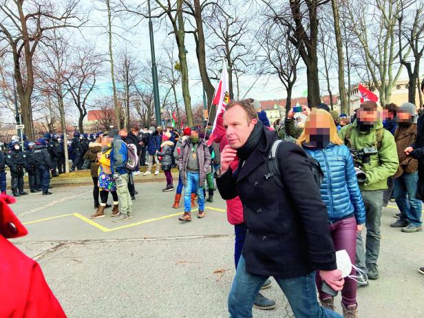 Eine Menschenmenge demonstriert auf einer Straße, im Hintergrund Polizisten.