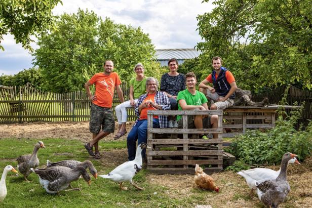 Die Familie Zoubek auf einer Wiese, umgeben von Gänsen und Hühnern