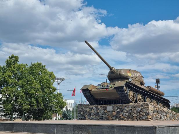 Ein 2. WKs Panzer steht auf einem Podest aus Steinen, dahinter ein Baum und Wolker.