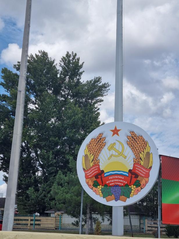 Ein Wappen mit Hammer und Sichel und sozialistischen Ährenkranz ist an einer Flaggenstange befestigt.