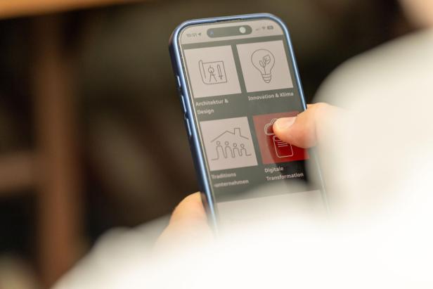 Ein Finger tippt auf dem Bildschirm eines Smartphones mit Icons zu Themen wie Architektur und Innovation.