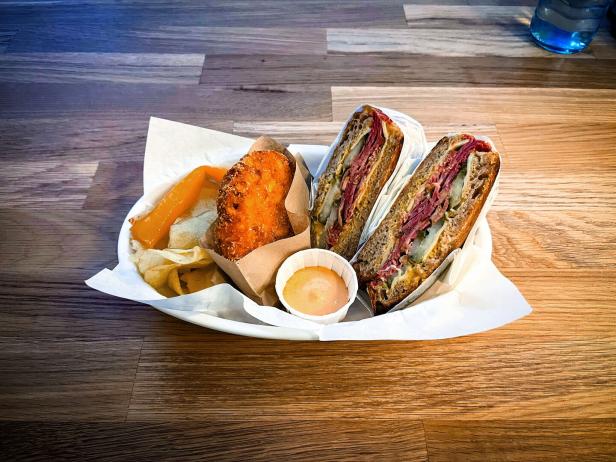 Das Bild zeigt ein Pastrami-Sandwich mit Chips und Hash Brown