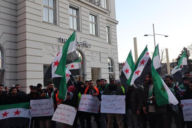 Personen demonstrieren, halten Syrien-Flaggen und Schilder hoch.