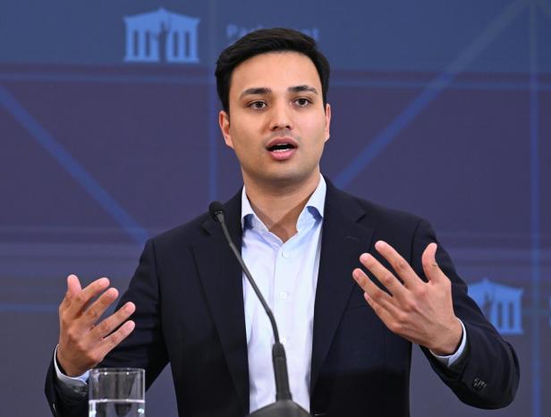 Ein Mann im Anzug, es ist Neos-Klubobmann Shetty, spricht gestikulierend an einem Mikrofon, vor ihm steht ein Glas Wasser.