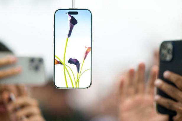 Ein iPhone Air hängt an Ladekabel ins Bild, dahinter stehen Menschen, die mit ihren Smartphones Fotos machen
