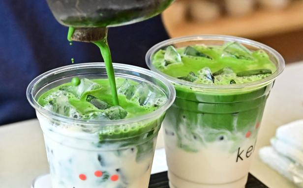 Zwei Plastikbecher, die mit Matcha-Latte befüllt werden