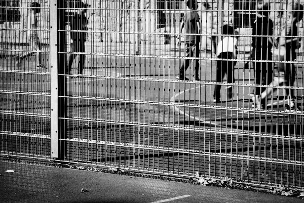 Mehrere Schüler bewegen sich hinter einem hohen Metallzaun auf einem Sportplatz.