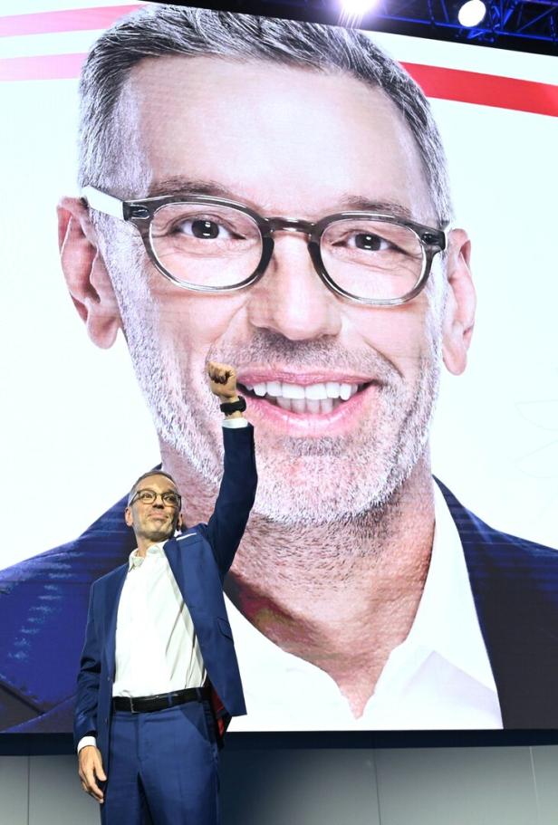 Ein Mann im Anzug, es ist FPÖ-Obmann Kickl, hebt die Faust vor einem riesigen Porträt seines eigenen Gesichts mit Brille und grauem Bart.
