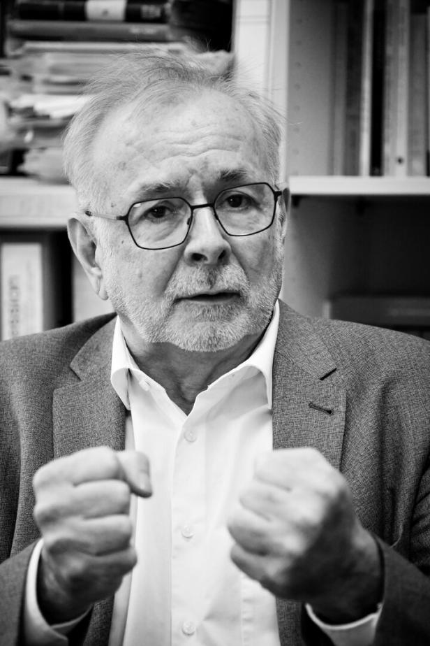 Ein Mann mit Brille und Anzug, der Historiker Rathkolb, ballt die Fäuste vor einem Bücherregal.