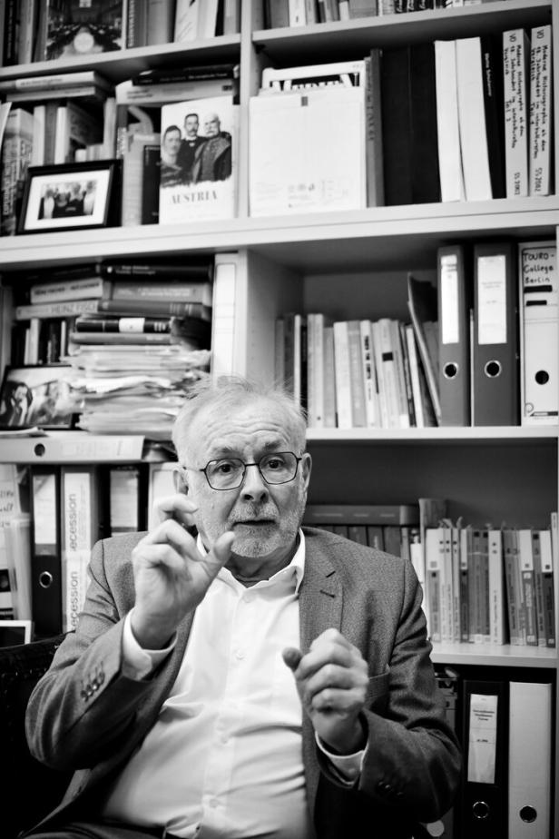 Ein Mann mit Brille, der Historiker Rathkolb, gestikuliert vor einem Bücherregal mit Ordnern der Touro-College Berlin.