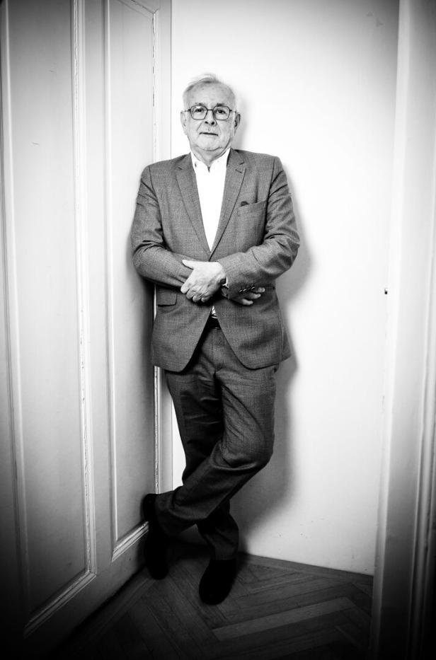 Ein Mann mit Brille und Anzug, der Historiker Rathkolb, lehnt an einer weißen Wand.