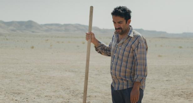 Der iranische Scahsupieler Vahid Mobasseri in einer Filmszene mit Schaufel in einer Wüstenlandschaft