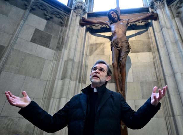 Ein Priester, der Wiener Erzbischof Grünwidl, steht mit offenen Armen vor einem Kruzifix in einer Kirche.