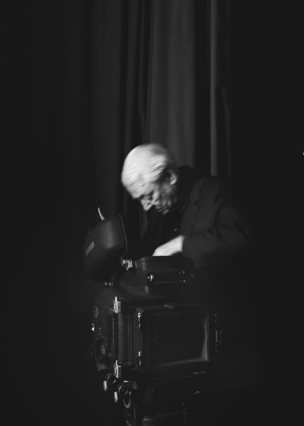 Der Künstler und Philosoph Alexander Kluge, wie er an einer Kamera arbeitet, in einer schwarzweißen Fotografie