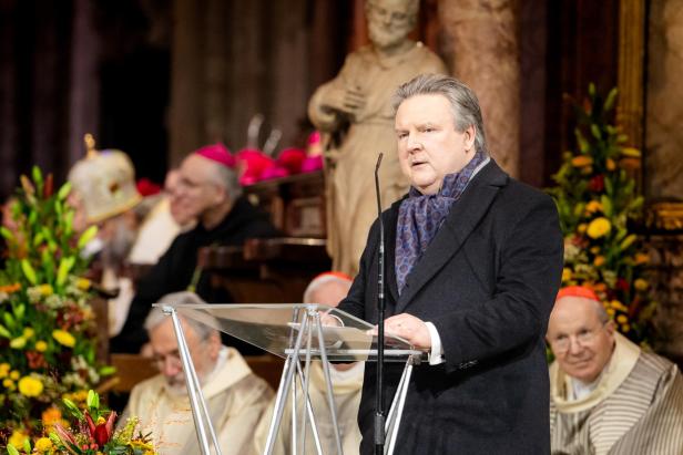 Ein Mann spricht in einer Kirche, hinter ihm sind Priester zu sehen